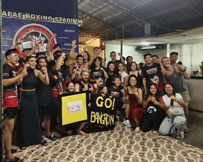 A group of people at a venue with a boxing ring and a sign that reads 'APAE Boxing Stadium.' 2