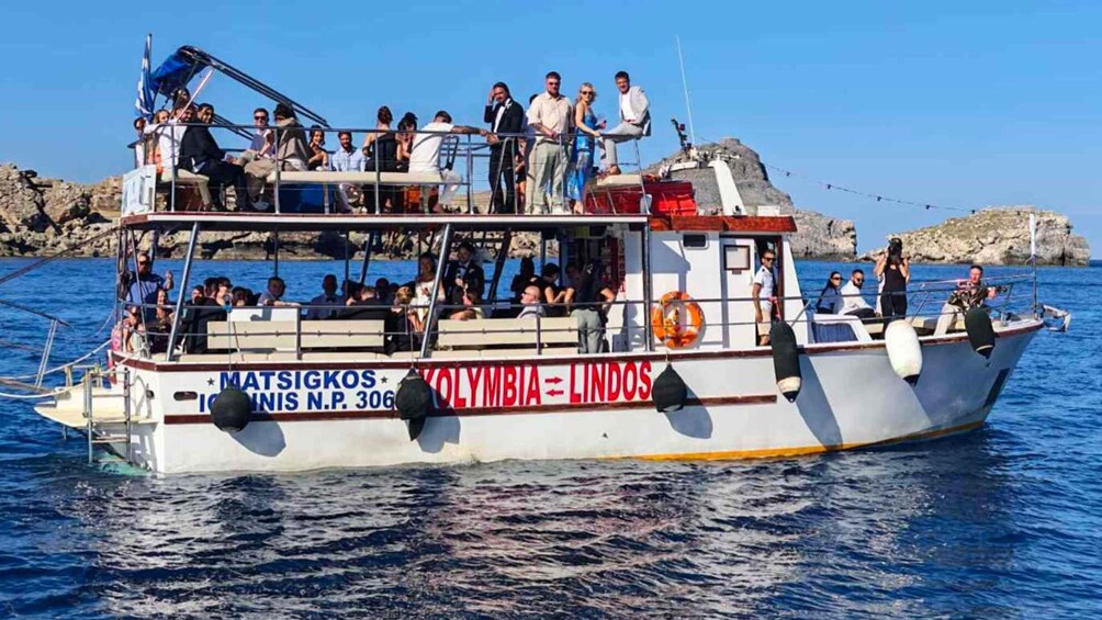 A boat with passengers, named 'MATSIGKOS,' on a body of water with rocky terrain in the background. 3