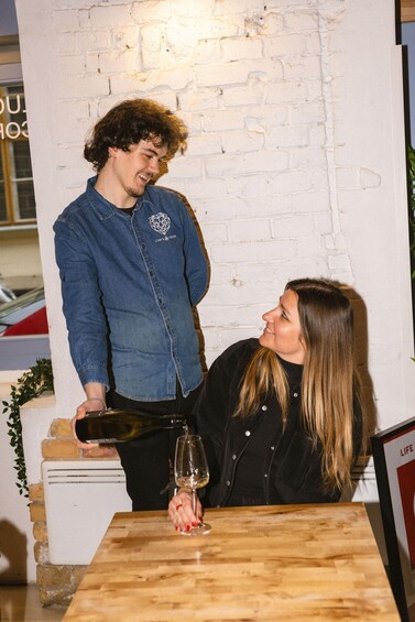 A person pouring wine into a glass at a wooden table with a brick wall background. 5