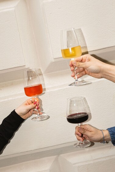 Two people holding wine glasses, one with red wine and the other with white wine, against a white wall. 3