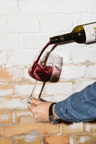 A person pouring red wine from a bottle into a glass. 4