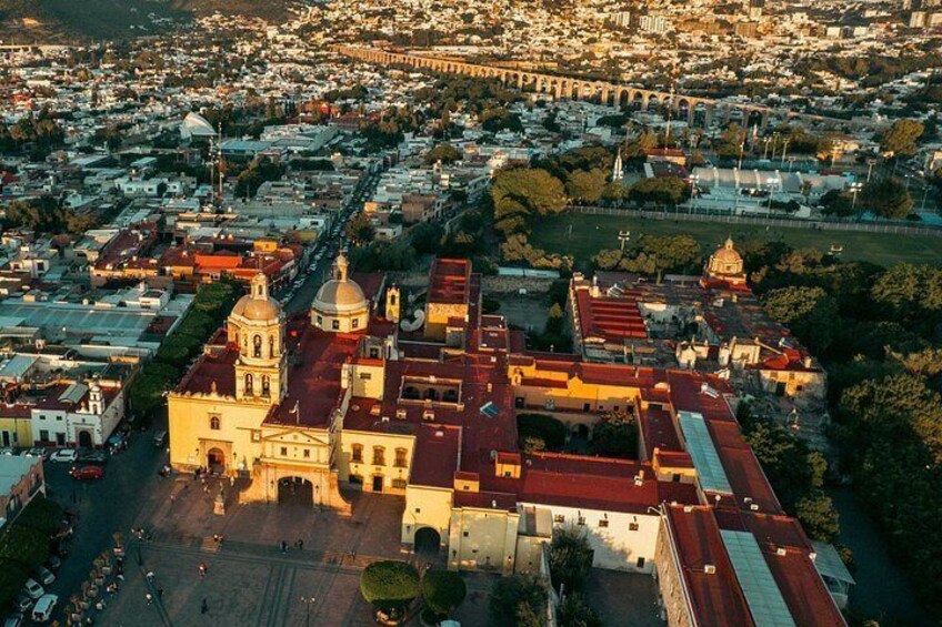 An aerial view of a city with a prominent cathedral, a large open square, and a bridge in the background. 1