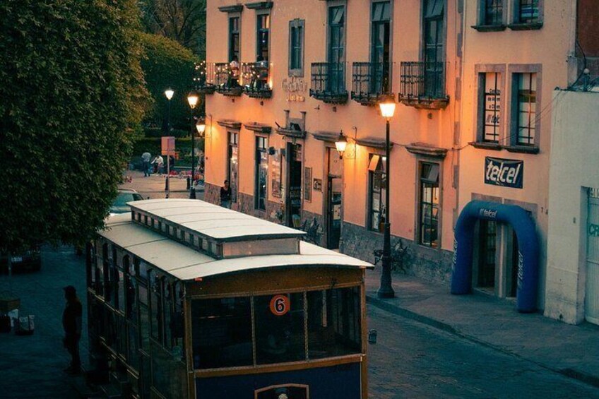 A vintage tram on a street with buildings and a sign that reads 'telcel'. 3