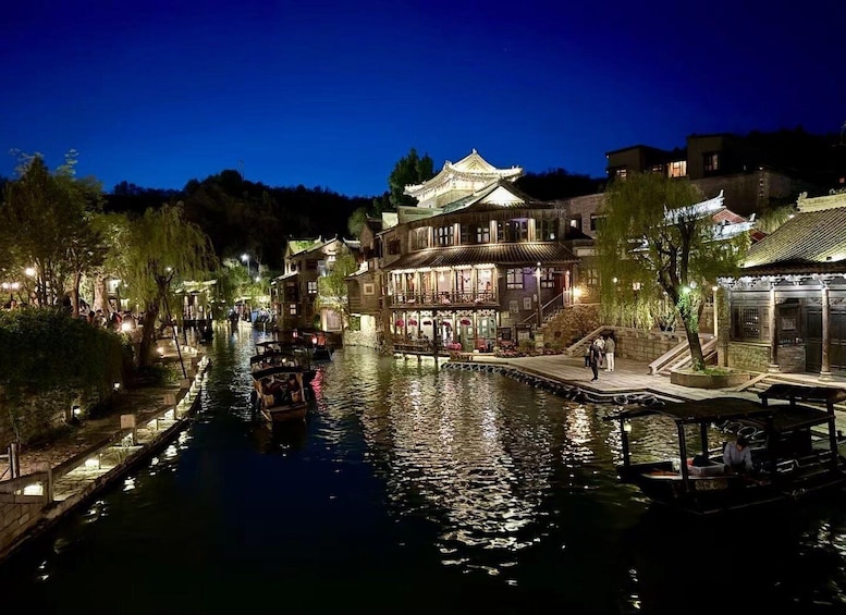 A traditional Chinese water town at night with illuminated buildings and boats on the water. 1