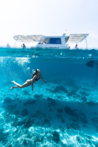 A person swimming underwater with a boat in the background. 1