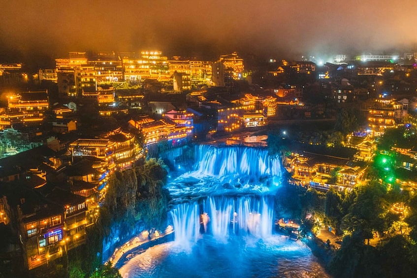 A night view of a town with illuminated buildings and a waterfall. 1