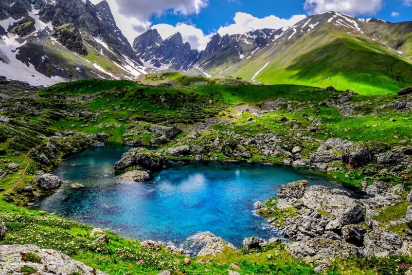A mountain landscape with a clear blue lake surrounded by rocky terrain and snow-capped peaks. 5