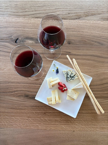 Two glasses of red wine, a plate with cheese and strawberries, and wooden chopsticks on a wooden table. 2