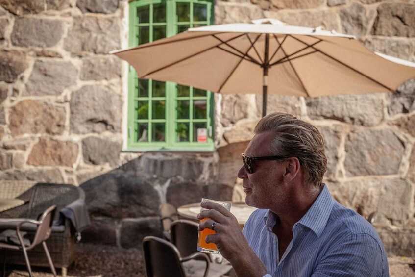 A man drinking from a glass at an outdoor table with a stone wall and a green window in the background. 5