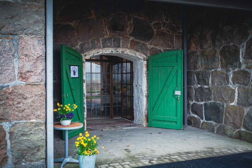 A stone building entrance with green doors, a small table with flowers, and a clear view into the interior. 2