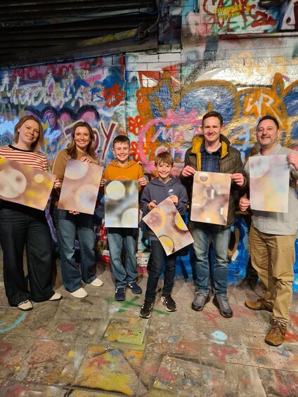 A group of people holding up translucent artwork against a graffiti-covered wall. 5