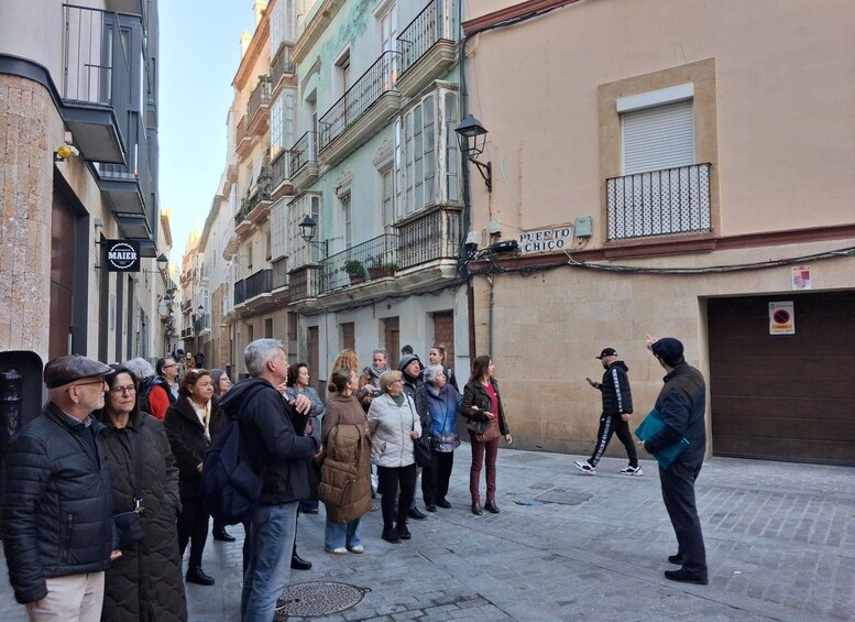 A group of people standing on a street, a man with a backpack walking by, and a building with a sign that reads 'PUERTO CHICO'. 2