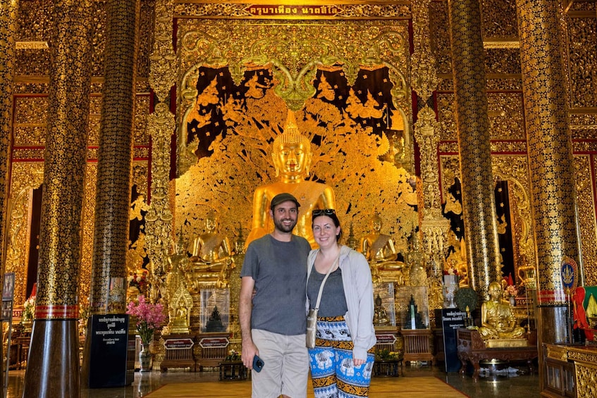 Kultainen Buddha-patsas temppelissä, jossa on monimutkaisia koristeita ja suuri kultainen katos. 1