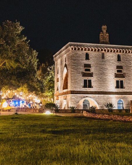 A historic stone building with arched windows and a tower, surrounded by a well-lit garden at night. 2
