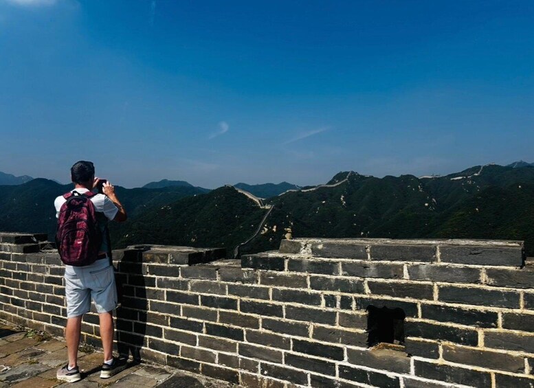 A person taking a photo of the Great Wall of China with mountains in the background. 3