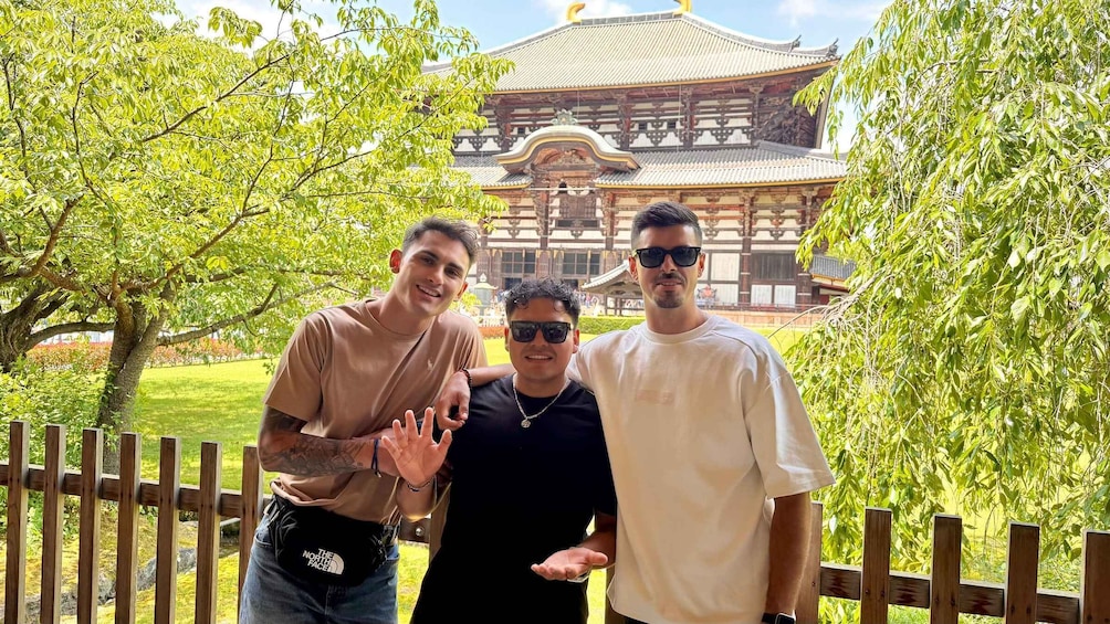 Three people standing in front of a traditional building with a tiled roof and wooden structure. 4