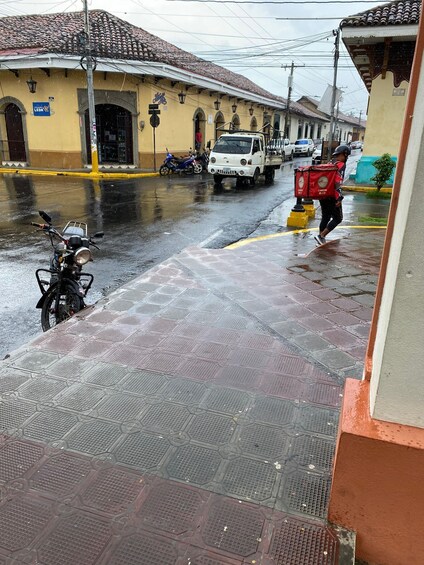 A wet street with a delivery person walking, a parked motorcycle, and a white truck. 5