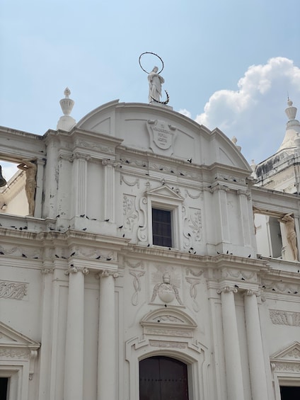 A white ornate building with a statue on top, a large arched window, and decorative carvings. 1