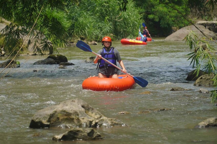 A person in a kayak navigating a river with rocks and vegetation. 5