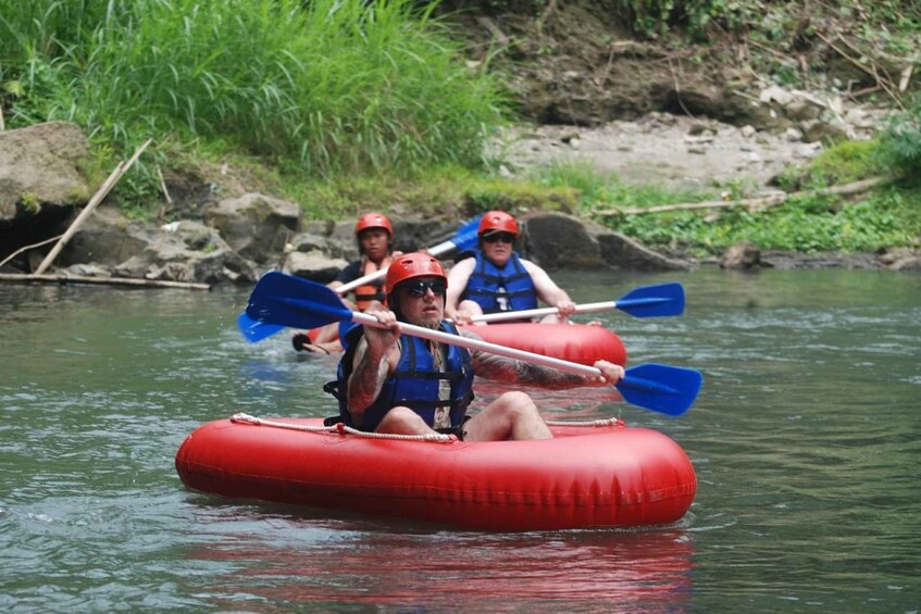 People in red inflatable rafts paddling down a river. 2