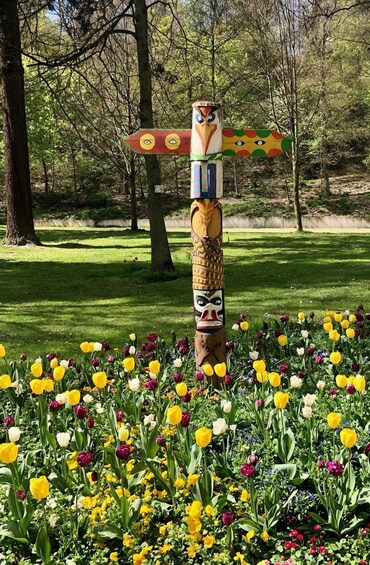 A totem pole with colorful carvings in a garden with tulips. 2