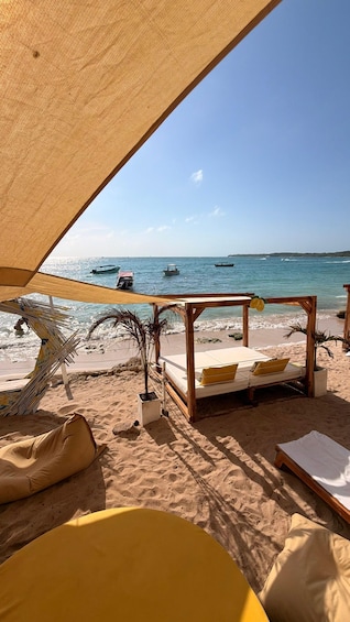 A beach with a wooden bed and a canopy, palm trees, and boats in the water. 5