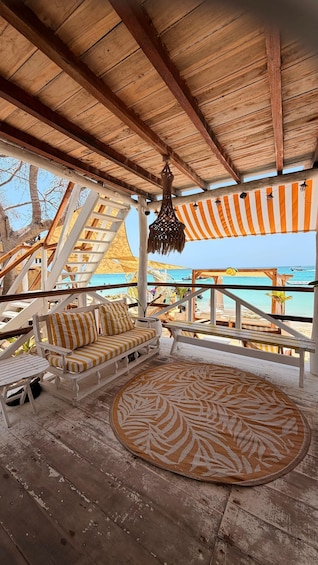 A wooden deck with striped cushions and a patterned rug, overlooking a beach. 4