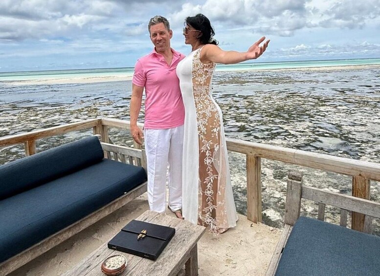A couple on a deck overlooking a beach with clear waters and a cloudy sky. 3
