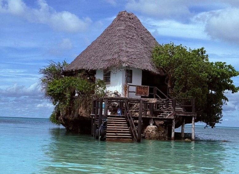 A thatched-roof house on stilts in clear turquoise water. 1