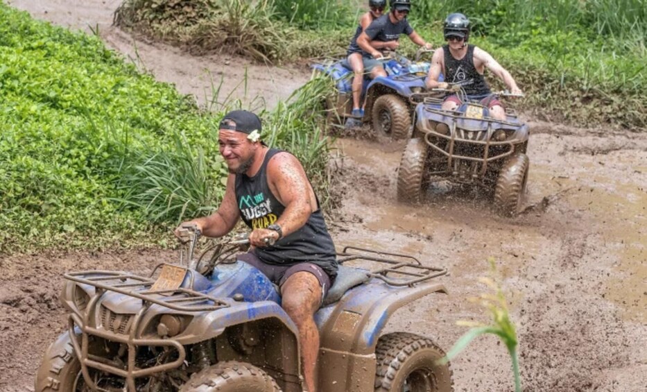A person riding a blue ATV on a muddy path with vegetation on the sides. 3