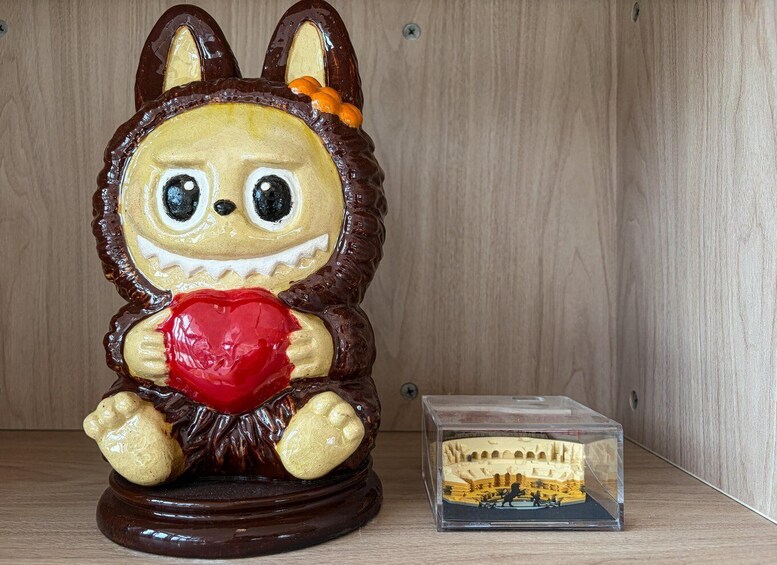 A ceramic rabbit figurine holding a red heart, next to a transparent display case with a miniature model of a building. 5