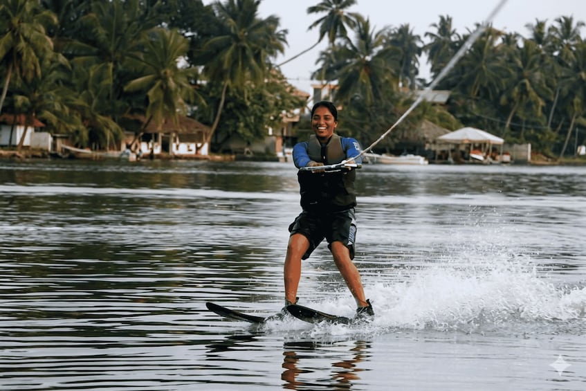 A person wakeboarding on a body of water with palm trees and buildings in the background. 1