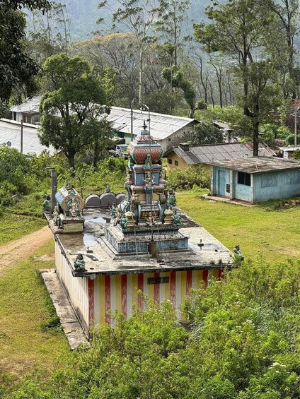 A traditional temple with a multi-tiered roof, surrounded by lush greenery and a few residential buildings in the background. 5