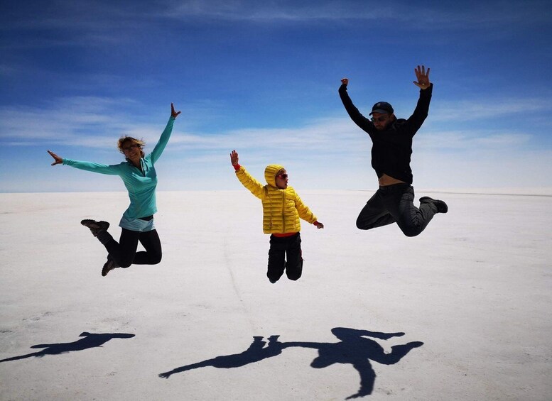 Three people jumping in a vast, flat, white landscape under a clear blue sky. 2