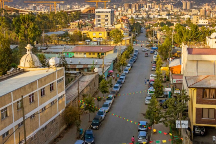 A city street lined with parked cars and buildings, with a bridge in the background. 3