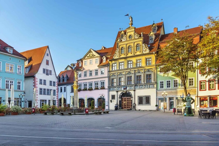 A European town square with colorful buildings, a statue, and outdoor seating. 1
