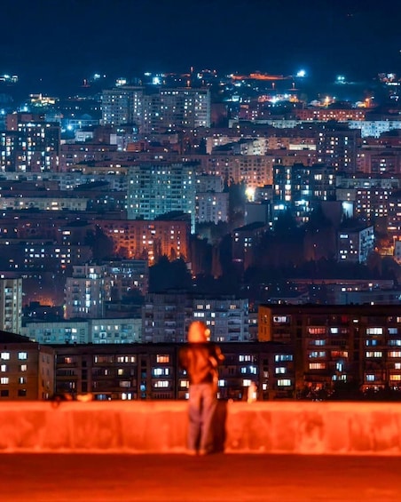 A nighttime cityscape with a person standing on a rooftop. 4