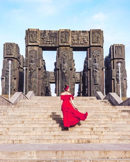 A person in a red dress descending a set of stone steps with intricate carvings and statues. 1