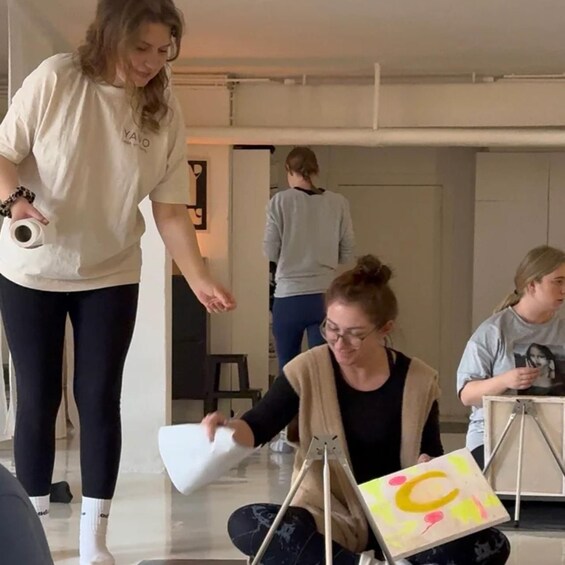 A person holding a roll of paper towels, another person sitting with a colorful painting, and a third person standing in the background. 4