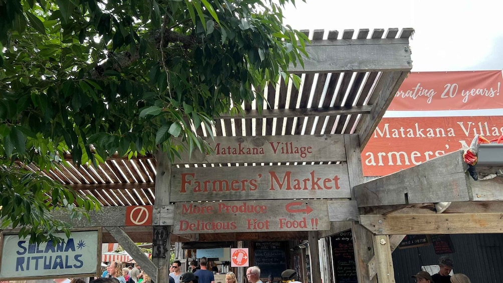 A wooden sign for Matakana Village Farmers' Market with a backdrop of trees and a red banner. 4