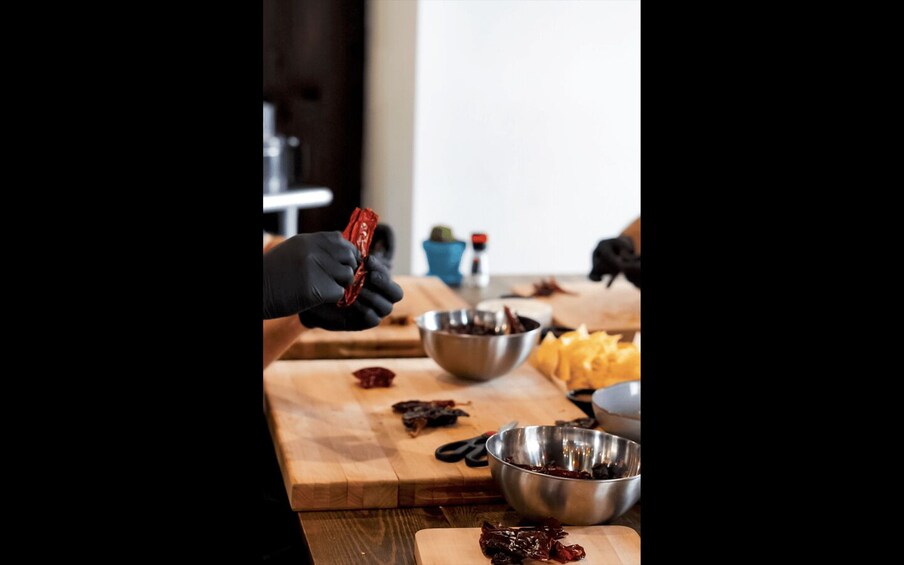 A person wearing gloves handling red peppers on a wooden cutting board with various kitchen items around. 2