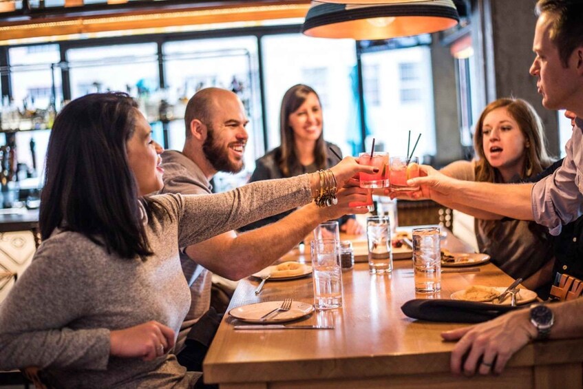 A group of people toasting with drinks at a bar with a wooden table and glasses. 1