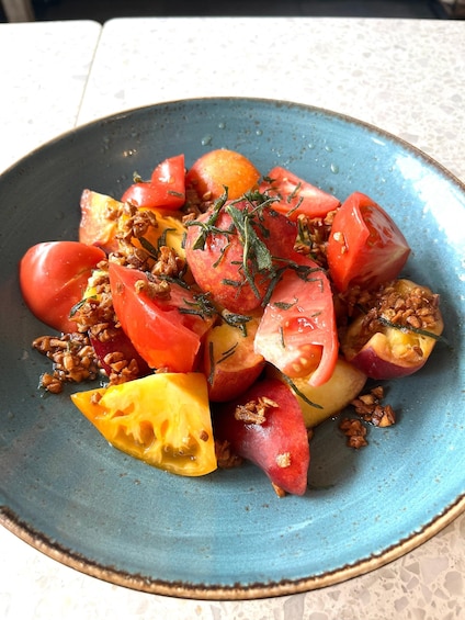 A blue ceramic plate with a salad of tomatoes, a yellow fruit, and walnuts, garnished with herbs. 2