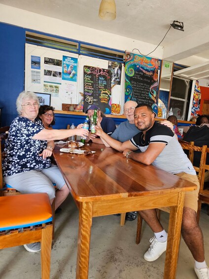 A group of people sitting around a wooden table in a casual dining setting with a menu board and various posters on the wall. 2