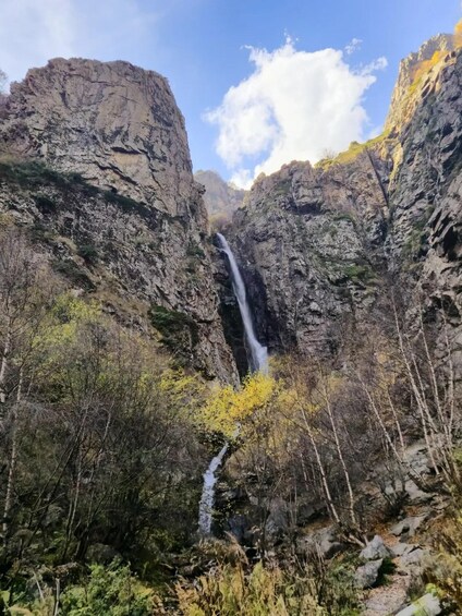 A waterfall in a rocky canyon with sparse vegetation and a clear sky. 1