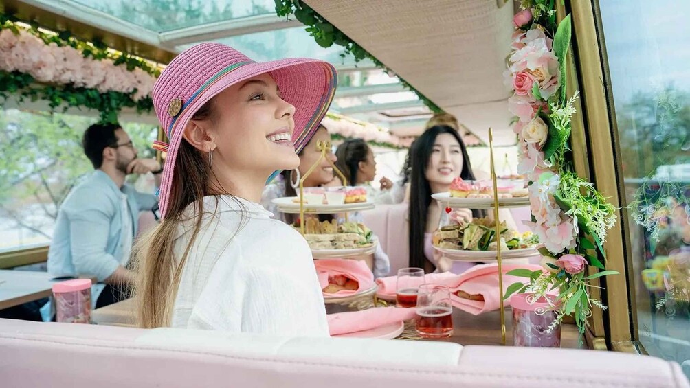 A person seated at a table with a pink hat, surrounded by floral decorations and a tiered dessert stand. 1