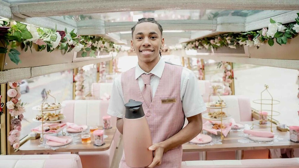 A person in a pink vest holding a black object, standing in a room with pink and white decor, including tables with food and flowers. 5