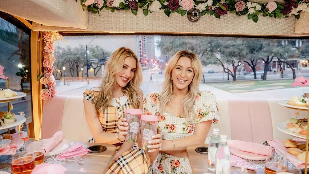 Two women seated at a table with floral decorations and a cityscape view. 3