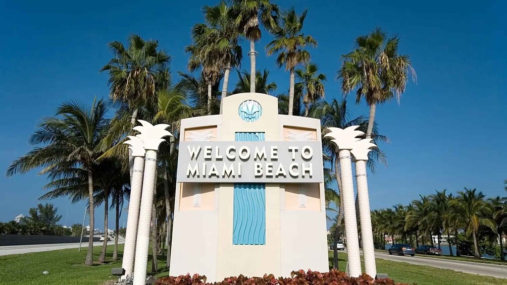 A sign welcoming visitors to Miami Beach with palm trees in the background. 2
