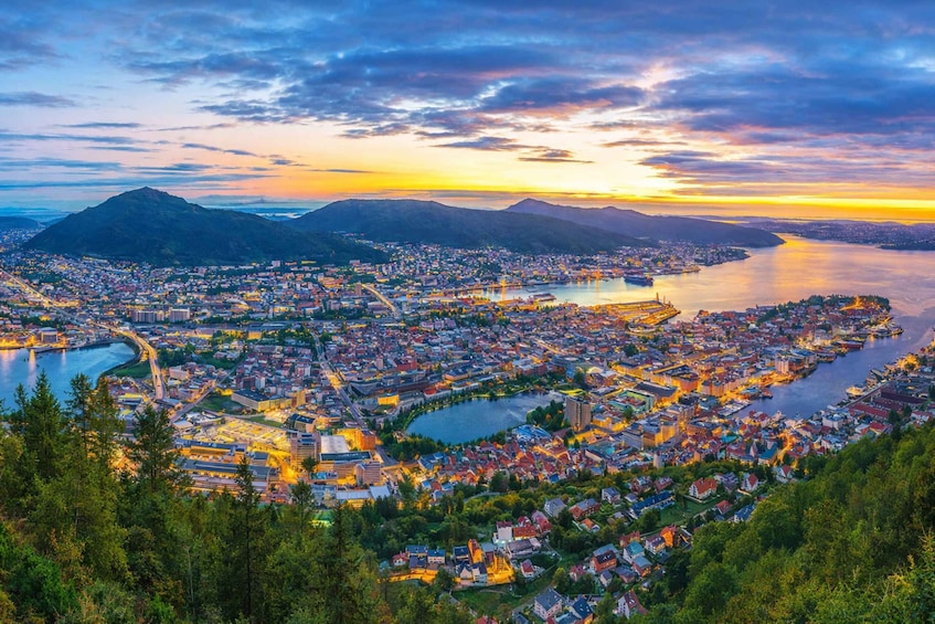 A panoramic view of a coastal city at sunset with a river, mountains, and a dense urban area. 4